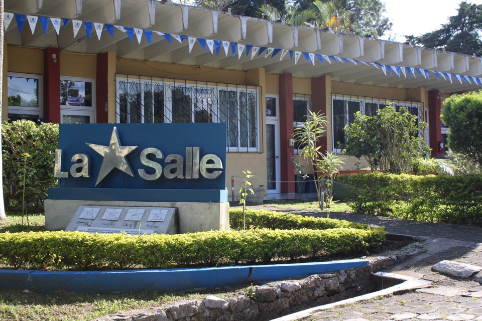 Letrero de La Salle entre jardines frente a los edificios del Instituto